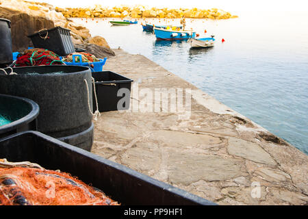 Villaggio di pescatori del Mediterraneo wharf con i tamburi e i contenitori pieni di reti da pesca con barche ormeggiate in background Foto Stock