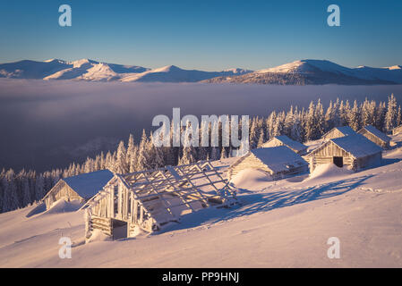 Paesaggio invernale con vecchie case di legno in montagna. Mattina di sole. Il villaggio di pastori Foto Stock