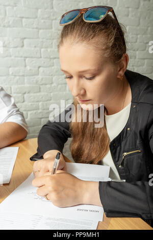 Una ragazza scrive un documento su un pezzo di carta. Foto Stock