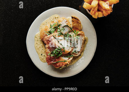 Delizioso merluzzo croccante su piatto bianco con patatine fritte in una ciotola con aceto di malto in polvere nel fresco ristorante londinese del tooting Market fish and chips Foto Stock