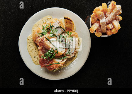 Delizioso merluzzo croccante su piatto bianco con patatine fritte in una ciotola con aceto di malto in polvere nel fresco ristorante londinese del tooting Market fish and chips Foto Stock