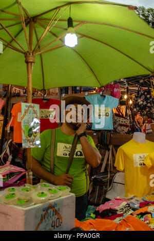 Merchant sul telefono di strada a piedi domenica Mercato Chiang Mai, Thailandia Foto Stock