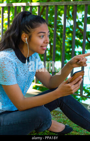 Ragazza seduta in un parco con lo smartphone - Mädchen, das in einem Park mit sitzt Smartphone - ragazza seduta in un parco con lo smartphone Foto Stock