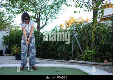 Ragazza giocare a minigolf, pronti a colpire la palla con un bastone Foto Stock