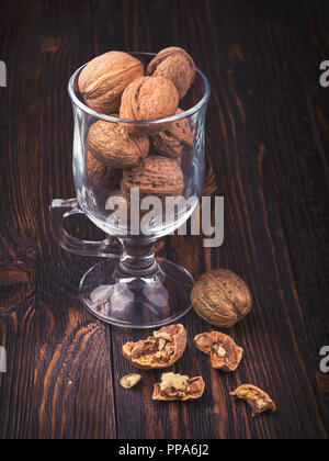 Gherigli di noce e le noci intere in un vetro al buio su un vecchio tavolo in legno Foto Stock