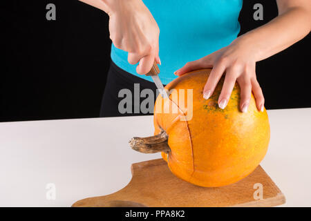 Ragazza mano taglia grande zucca arancione sul pannello di legno isolato su sfondo nero. Halloween e la Giornata del Ringraziamento food concept. Close up Foto Stock