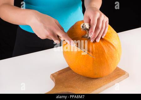 Donna tagli e preparare arancione zucca di Halloween sulla tavola di legno e scrivania con il coltello. Halloween e la Giornata del Ringraziamento food concept. Close up Foto Stock