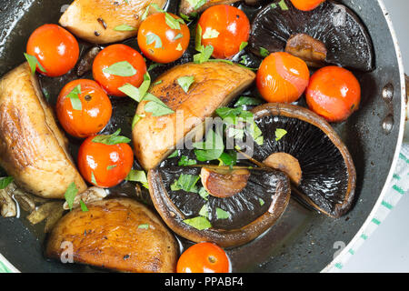 I funghi e i pomodori ciliegia essendo agitare fritto in un poco profondo la padella, guarnite con prezzemolo fresco tritato Foto Stock