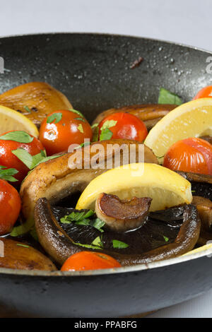 I funghi e i pomodori ciliegia essendo agitare fritto in un poco profondo la padella, guarnite con prezzemolo fresco tritato e spicchi di limone Foto Stock