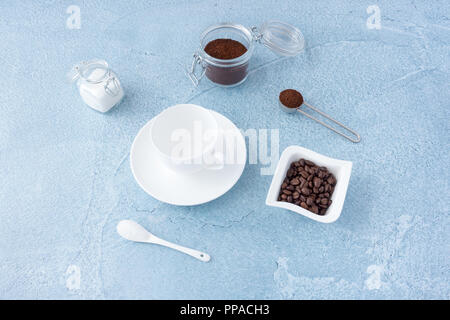 Concetto di caffè vuote con tazza di caffè, lo zucchero bianco e il caffè macinato in vasetti di vetro blu su sfondo di calcestruzzo. Foto Stock