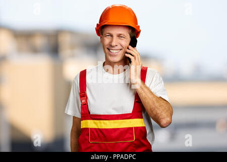 Felice lavoratore in elmetto parlando al telefono. Foto Stock