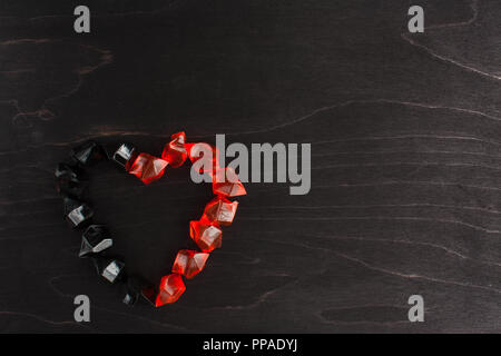 Cuore di colore arancione e nero gemme di plastica su un nero lo sfondo di legno Foto Stock