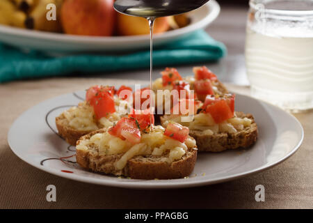 Close-up di cucchiaio versando olio d'oliva in un bruschette con mozzarella, pomodoro e origano; messa a fuoco selettiva. Foto Stock