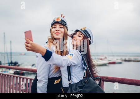 Due college studenti donne di Marine Academy tenendo selfie dal mare indossando uniforme. Happy amici divertendosi sul molo Foto Stock