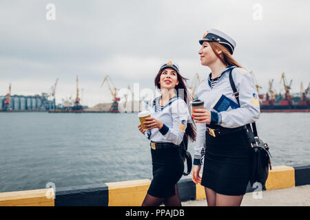 Due college studenti donne di Marine Academy a piedi dal mare indossando uniforme. Amici camminare, parlare e bere caffè Foto Stock