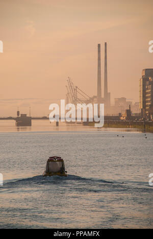 Alba sul fiume Liffey con vista alla Dublin Docklands con barca e landmark twin camini di Poolbeg potenza nel retro. Foto Stock