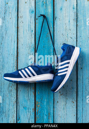 Coppia di maschio blu sneakers tessili sospesi su stringhe su un blu parete in legno Foto Stock