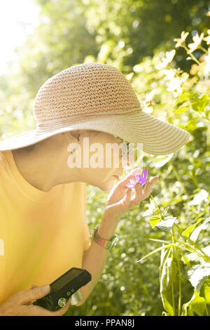 Una donna sola, passeggiate nel parco o giardino, prende le immagini e profuma di fiori, ella è giovane pensionato e lei gode di natura. Foto Stock