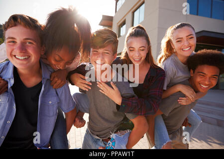 Ritratto di alta scuola gli studenti dando a ogni altra piggyback College di edifici Foto Stock