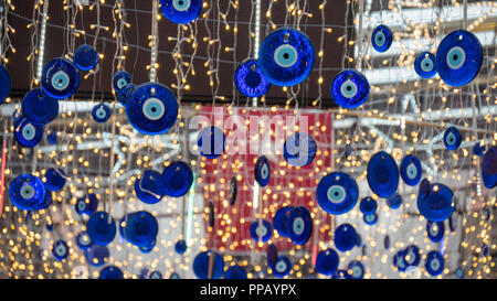 Close up occhi blu a forma di amuleti chiamati occhio cattivo o Nazar. Impiccati sul tetto. Sfocata bandiera turca e le luci a led su sfondo. Foto Stock