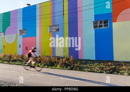 In rapido movimento di ciclista passando da un colorato parete dipinta sul Arbutus Greenway, Kitsilano, Vancouver, BC, Canada Foto Stock