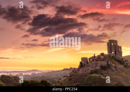 Corfe Castle, Dorset. Il 25 settembre 2018. Regno Unito - Previsioni del tempo - Dopo una notte fredda, un colorato tramonto sull'storiche rovine di Corfe Castle araldi di inizio a temperature crescenti nella contea di Dorset, Inghilterra. Credito: Terry Mathews/Alamy Live News Foto Stock
