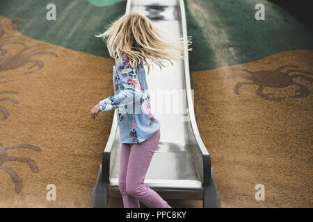 Ragazza bionda rivolto lontano sulla slitta nel parco giochi Foto Stock