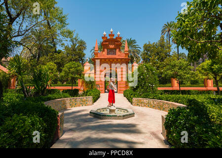 Giovane donna in abito rosso nei giardini dell'Alcazar, fontana, Royal Palace di Sevilla, Sevilla, Spagna Foto Stock
