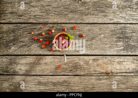 Vista dall'alto di deliziosi piatti fatti in casa confettura di fragole servito in una ciotola di legno decorato con foglie di menta fresca e fresche fragole mature sparsi intorno Foto Stock