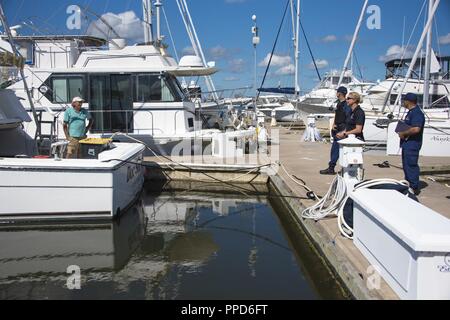 Lt. La Cmdr. Kerry duca, un indagando officer presso Coast Guard Settore Charleston, Bridget Wyant, una guardia costiera agente speciale, e Sottufficiali terza classe Casy Strawn, una di boatswain mate alla Stazione della Guardia Costiera Charleston, discutere illegale e charter nautica con sicurezza proprietario di imbarcazione 30 agosto 2018, presso il porto di Charleston Marina a Charleston, Carolina del Sud. Il duca, Wyant e Strawn camminato i docks di vari porti in tutta Charleston per educare il pubblico su illecita charter nautica e sicurezza. Foto Stock