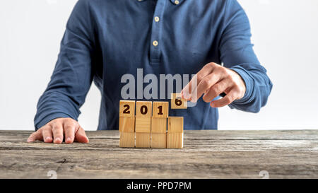 Vista frontale di un uomo di assemblaggio di un 2016 segno con cubetti di legno come progetta il suo futuro e decide della sua risoluzione di nuovi anni. Foto Stock