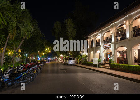 Parcheggiato scooter, lit francese di epoca coloniale edificio e lanterne appese in alberi su un idilliaco Sakkaline Road a Luang Prabang, Laos, al tramonto. Foto Stock