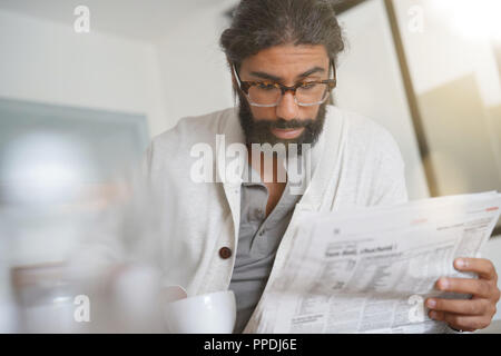 Dai capelli scuri uomo barbuto a casa leggere il giornale Foto Stock