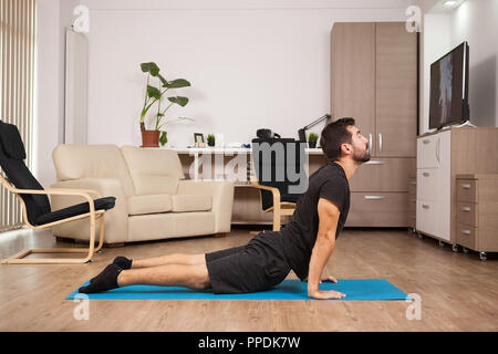 I giovani adulti facendo yoga cobra pongono sulla sua casa piano. Home te Foto Stock