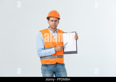 Frustrati giovane ingegnere con casco e giubbotto del controllo di errore nel documento sopra uno sfondo grigio Foto Stock