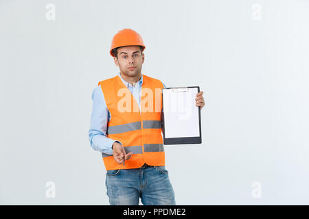 Frustrati giovane ingegnere con casco e giubbotto del controllo di errore nel documento sopra uno sfondo grigio Foto Stock