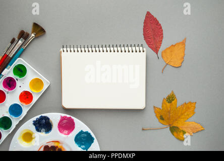 Piatto di laici acquerello tavolozza, pennelli, notepad e foglie di autunno. Ciao autunno del concetto. Foto Stock
