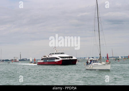 Jet rosso 4 in catamarano e barca a vela bianca con le vele verso il basso avvicinandosi Cowes, Isle of Wight, Regno Unito Foto Stock