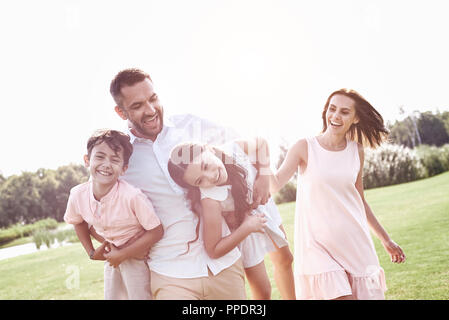 L'incollaggio. Famiglia di quattro camminando sul campo erboso padre portante Foto Stock