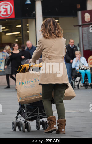 Una donna spingendo una carrozzina caricato con Primark borse per lo shopping. Foto Stock