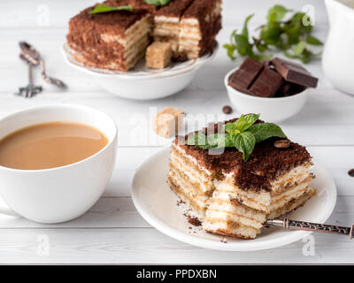 Il tiramisù Dessert con menta e tazza di caffè bianco su un tavolo di legno. Foto Stock