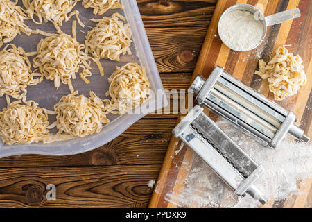 In casa fettuccine essendo preparati in una cucina con una vista aerea di porzioni di pasta fresca essiccazione su un vassoio e un metallo taglia pasta su un Foto Stock