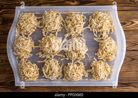 Fasci o porzioni di freschi fettuccine essiccazione su un bianco vassoio di plastica su un tavolo da cucina in casa o in un ristorante vista dal di sopra in un piatto la Foto Stock