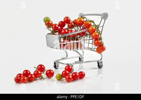 Mini carrello pieno con pomodori ciliegia su sfondo bianco. Spazio di copia Foto Stock