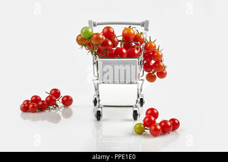 Mini carrello pieno con pomodori ciliegia su sfondo bianco. Spazio di copia Foto Stock