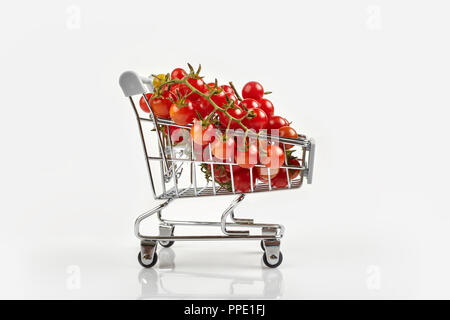 Mini carrello pieno con pomodori ciliegia su sfondo bianco. Spazio di copia Foto Stock