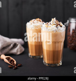 Iced latte caffè in un bicchiere alto con caramello e lo sciroppo al cioccolato e panna montata. Legno scuro dello sfondo. Foto Stock
