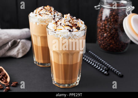 Iced caramello latte caffè in un bicchiere alto con lo sciroppo al cioccolato e panna montata. Sfondo scuro. Foto Stock