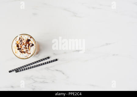 Vista superiore del latte ghiacciata caffè in un bicchiere alto con caramello e sciroppo di cioccolato sulla panna montata. In marmo bianco con sfondo spazio copia. Foto Stock