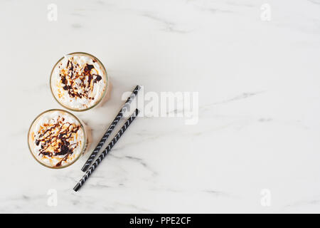 Vista dall'alto di due caffè ghiacciato in un bicchiere alto con caramello e sciroppo di cioccolato sulla panna montata e due cannucce. In marmo bianco con sfondo spazio copia. Foto Stock
